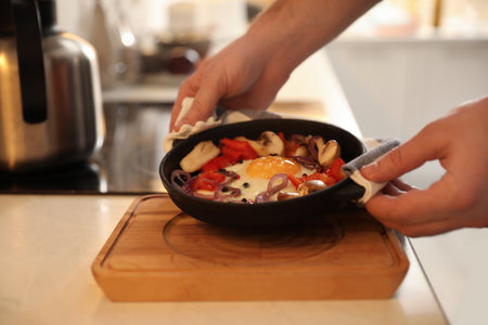 Man frying pan with fresh putting egg and vegetables on wooden board, closeupの写真素材