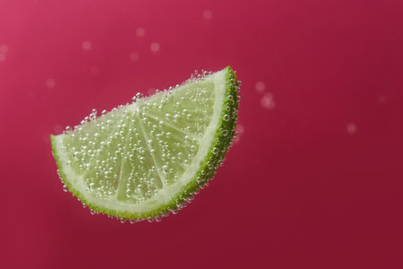 Slice of lime in sparkling water on dark pink background, space for text. Citrus sodaの写真素材