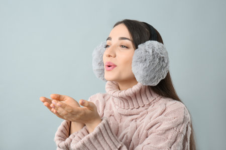 Beautiful young woman wearing earmuffs on light gray backgroundの写真素材
