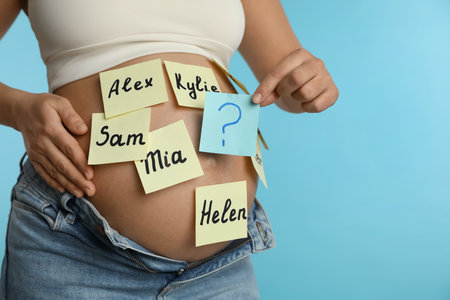Pregnant woman with different baby names on belly against light blue background, closeupの写真素材