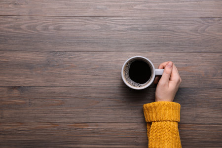 Woman with cup of coffee at wooden table, top view. Space for textの写真素材