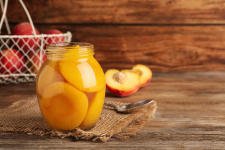 Canned peach halves in glass jar on wooden table, space for textの写真素材