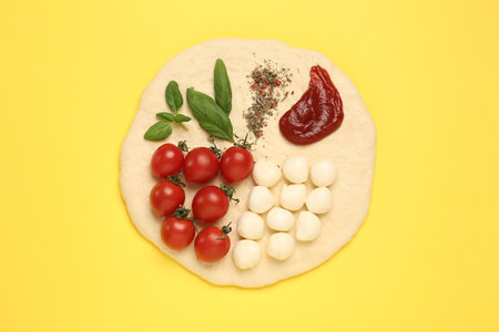 Raw dough and other ingredients for pizza on yellow background, top viewの写真素材