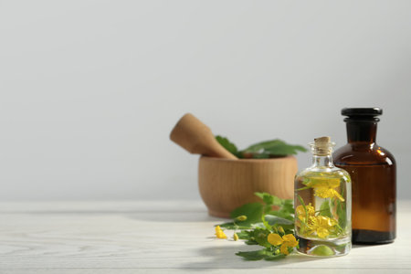 Bottles of celandine tincture and plant on white wooden table, space for textの写真素材