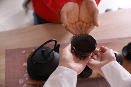 Master giving freshly brewed beverage to guest during traditional tea ceremony at table, closeupの写真素材