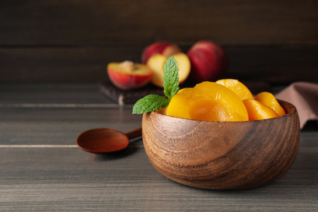 Canned peach halves in bowl on wooden table, space for textの写真素材