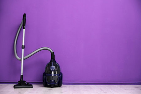 Modern vacuum cleaner near purple wall indoors, space for textの写真素材