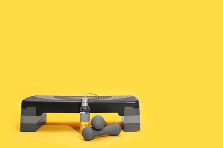 Step platform, dumbbells and bottle of water on yellow background, space for text. sports equipmentの写真素材