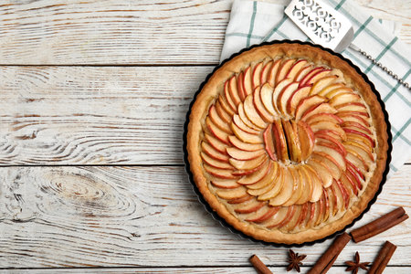Delicious homemade apple tart, cinnamon, anise and cake shovel on white wooden table, flat lay. Space for textの写真素材