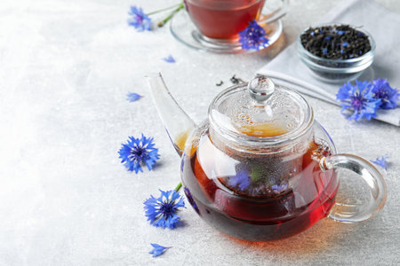 Glass pot with tea and cornflowers on light table. Space for textの写真素材