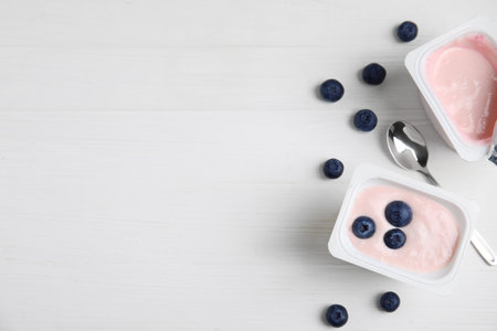 Plastic cups with tasty yogurts and blueberries on white wooden table, flat lay. Space for textの写真素材