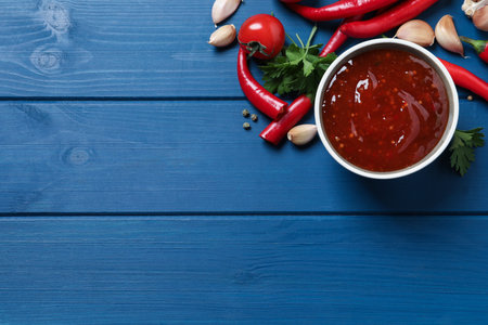 Spicy chili sauce and ingredients on blue wooden table, flat lay. Space for textの写真素材