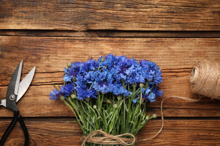 Bouquet of beautiful cornflowers with scissors and twine on wooden table, flat layの写真素材