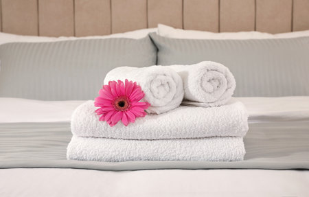 Fresh white towels with flower on bed indoorsの写真素材