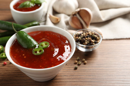 Spicy chili sauce in bowl on wooden table, space for text