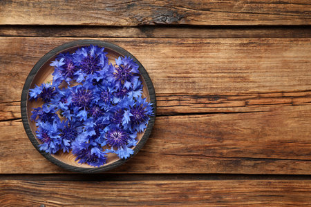 Beautiful blue cornflowers in bowl on wooden table, top view. Space for textの写真素材