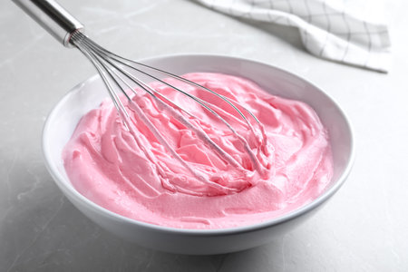 Whipping pink cream with balloon whisk on light gray table, closeupの写真素材