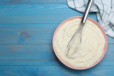 Pastry cream with balloon whisk on light blue wooden table, flat lay. Space for textの写真素材