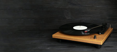 Turntable with vinyl record on black wooden background. Space for text