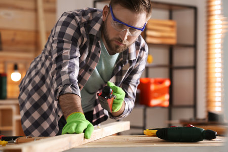 Carpenter shaping wooden bar with hand plane at table in workshopの写真素材