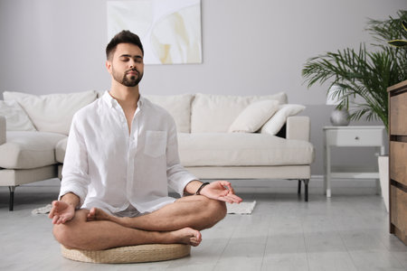 Young man meditating on straw cushion at home, space for textの写真素材