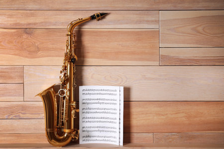 Beautiful saxophone and note sheets on table near wooden wall, space for textの写真素材