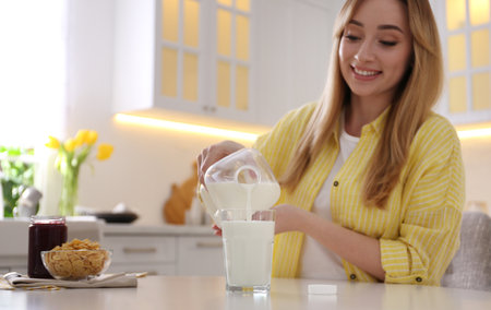 Young woman pouring milk from gallon bottle into glass at white table in kitchenの写真素材