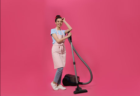 Housewife with vacuum cleaner on pink backgroundの写真素材