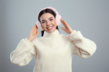 Beautiful young woman wearing earmuffs on light gray backgroundの写真素材
