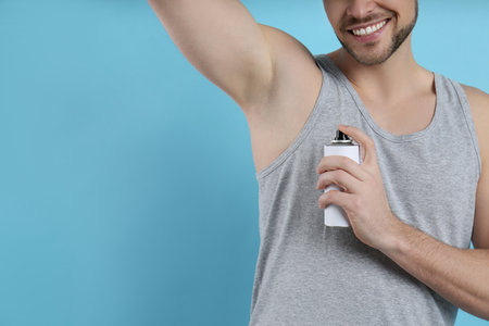 Man applying deodorant on turquoise background, closeup. Space for textの写真素材