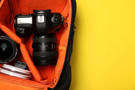 Camera in photographer's backpack on yellow background, top view. Space for textの写真素材