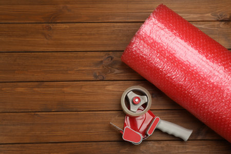 Bubble wrap roll and tape dispenser on wooden background, flat lay. Space for textの写真素材
