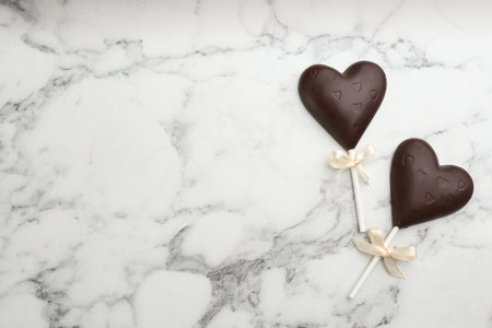 Chocolate heart shaped lollipops on white marble table, flat lay. Space for textの写真素材