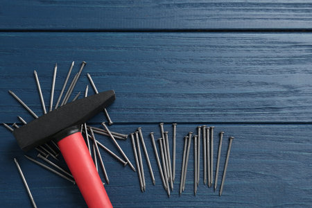Hammer and metal nails on blue wooden table, flat lay. Space for text