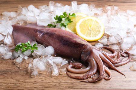 Fresh raw squid with ice, lemon and parsley on wooden tableの写真素材