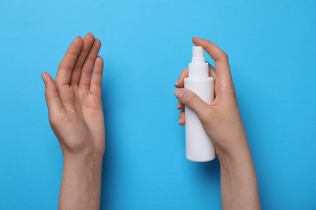 Woman spraying antiseptic onto hand on light blue background, closeup. safety equipmentの写真素材