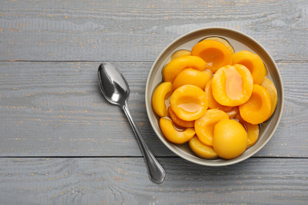 Canned peach halves and spoon on gray wooden table, flat lay. Space for textの写真素材