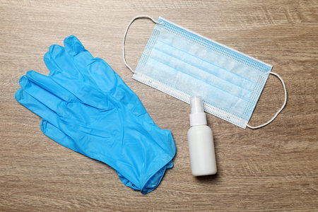 Medical gloves, mask and hand sanitizer on wooden background, flat lay. safety equipment