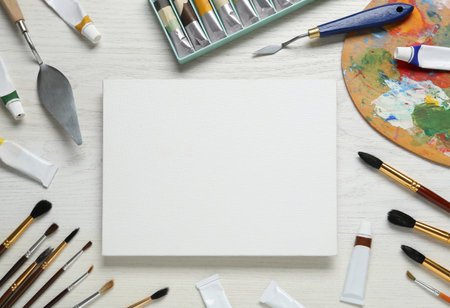 Blank canvas, tools, palette and paints on white wooden table, flat lay. Space for textの写真素材