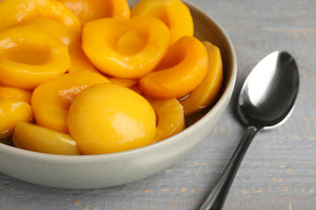 Canned peach halves and spoon on gray wooden table, closeupの写真素材