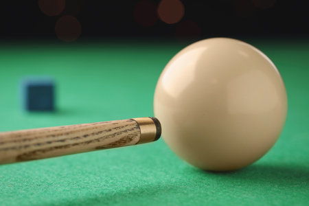 Classic plain billiard ball and cue on green table, closeup