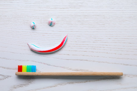 Funny face made with toothpaste and brush on white wooden background, flat lay
