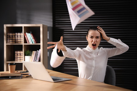 Emotional young businesswoman throwing papers at table in office. Hate and burnout conceptの写真素材