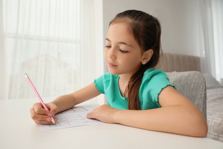 Little girl solving sudoku puzzle at table indoorsの写真素材
