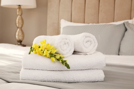 Fresh white towels with flower on bed indoorsの写真素材