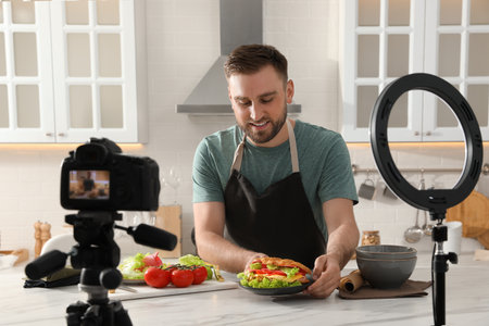 Blogger with tasty croissant recording video in kitchen at home. Using ring lamp and cameraの写真素材