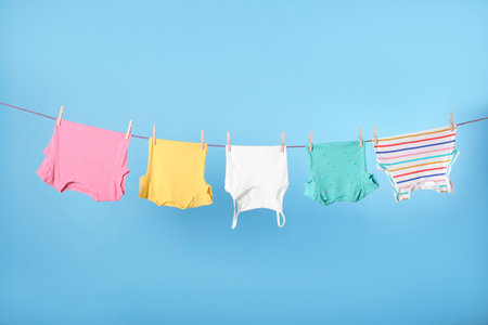 Clean child's clothes hanging on laundry line against light blue backgroundの写真素材