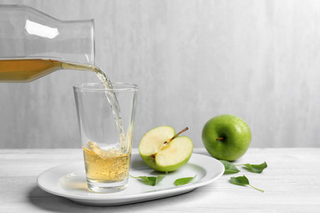 Pouring fresh apple juice into glass on white wooden tableの写真素材