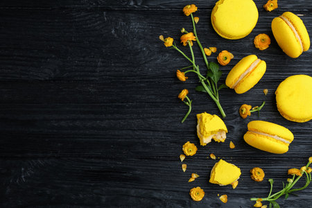 Flat lay composition with delicious yellow macarons and flowers on black wooden table. Space for textの写真素材