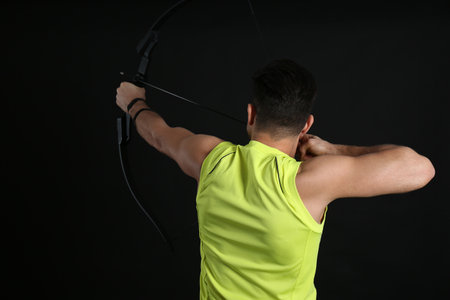 Man with bow and arrow practicing archery on black background, back viewの写真素材